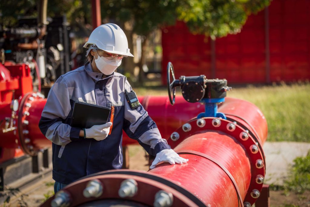 Engineer inspecting red pipeline with butterfly valve at water treatment plant