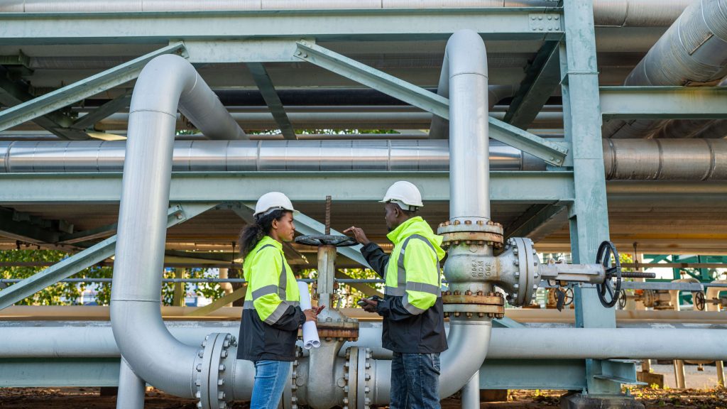 Engineers inspecting a large industrial valve in a process plant with visible piping systems.