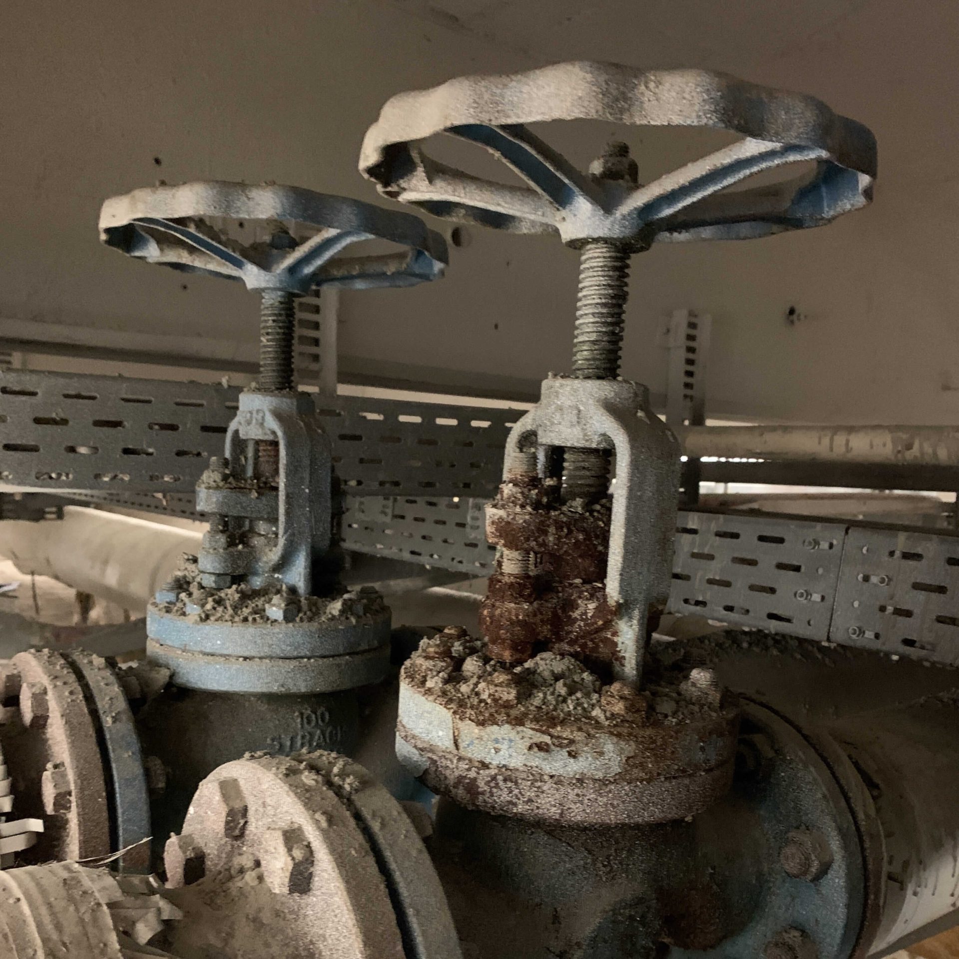 Rusty gate valves covered in corrosion and dust inside an industrial piping system.