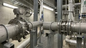 Photorealistic industrial pipeline scene showing a lugged vs wafer butterfly valve comparison with two butterfly valves installed in a metal piping system inside a modern processing facility.