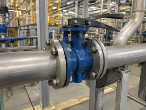 Butterfly valve characteristics shown through a compact industrial butterfly valve installed in a large process piping system, with the valve body, actuator, and surrounding industrial environment clearly visible.