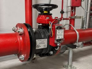 butterfly valve tamper switch installed on a fire protection piping system, showing the supervised valve assembly in a realistic facility environment with control equipment nearby