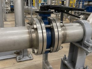 butterfly valve wafer type installed in an industrial piping system with flanges, actuator, and surrounding equipment in a realistic mechanical environment