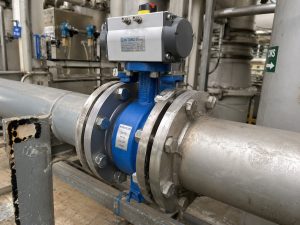Butterfly Wafer Valve installed between pipeline flanges in an industrial process environment, showing the valve body, actuator, connected piping, and a technical procurement inspection scene.